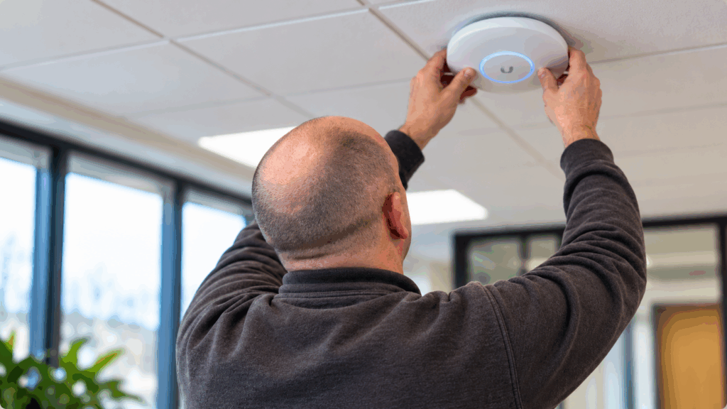 Technician installing a WiFi access point on an office ceiling